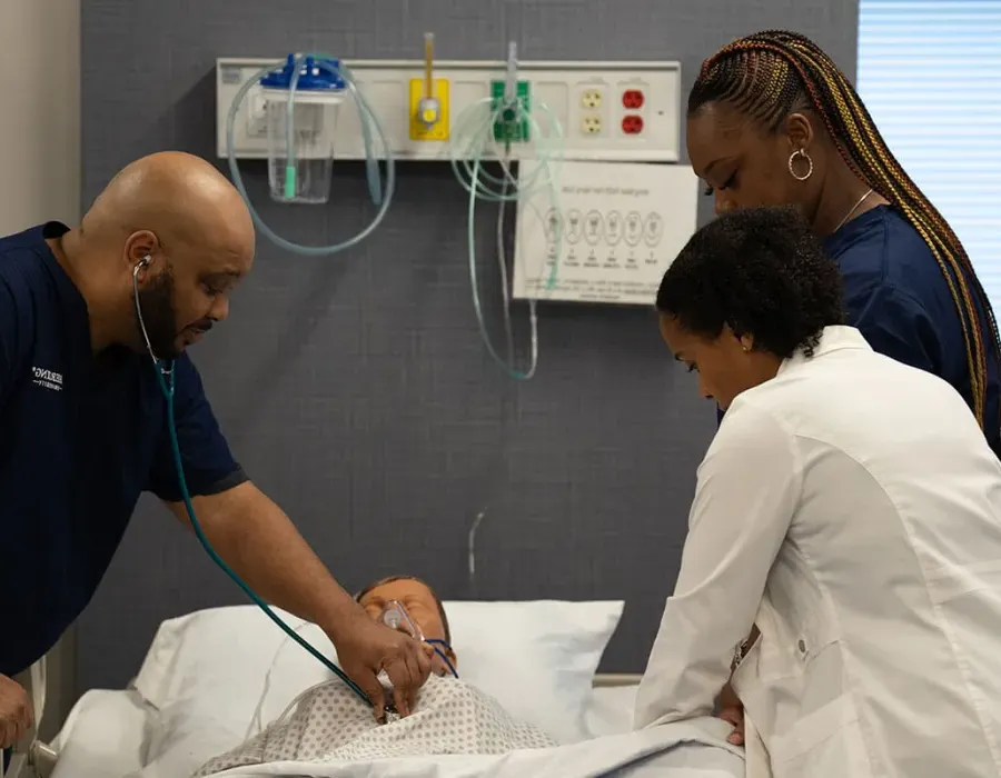 Herzing nursing students practicing reading heart rate with nursing instructor during simulation lab